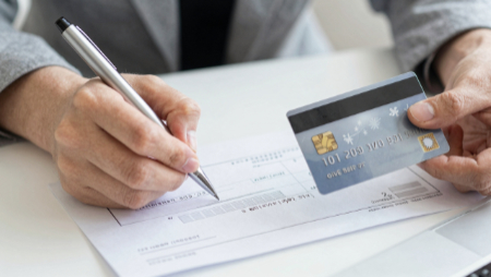 hand holding pen writing check debit card in other hand